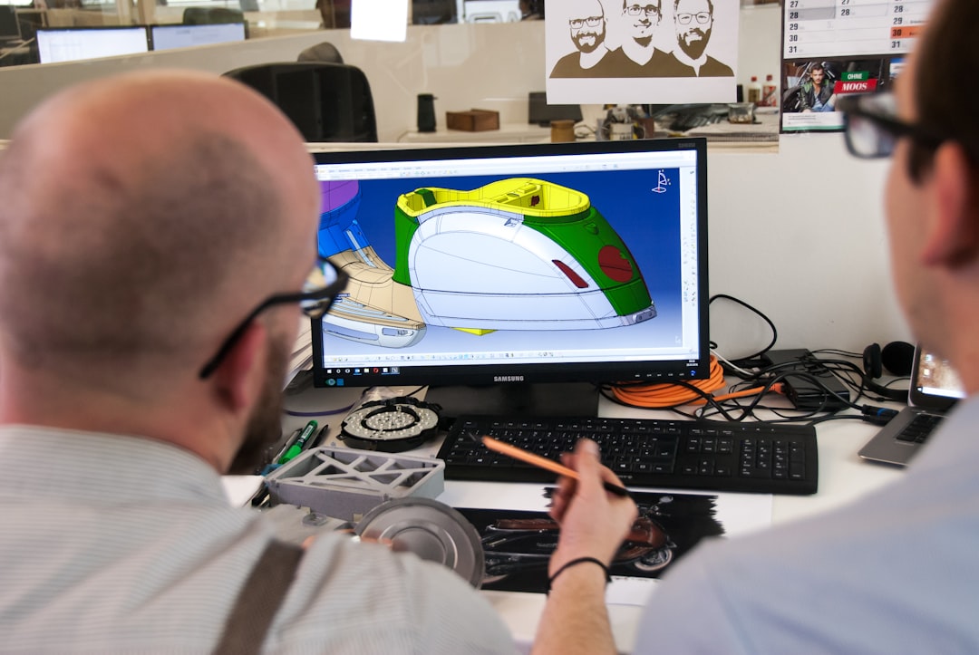 man in white shirt wearing black framed eyeglasses team collaborating on 3D model, cloud based design software, multiple screens workspace