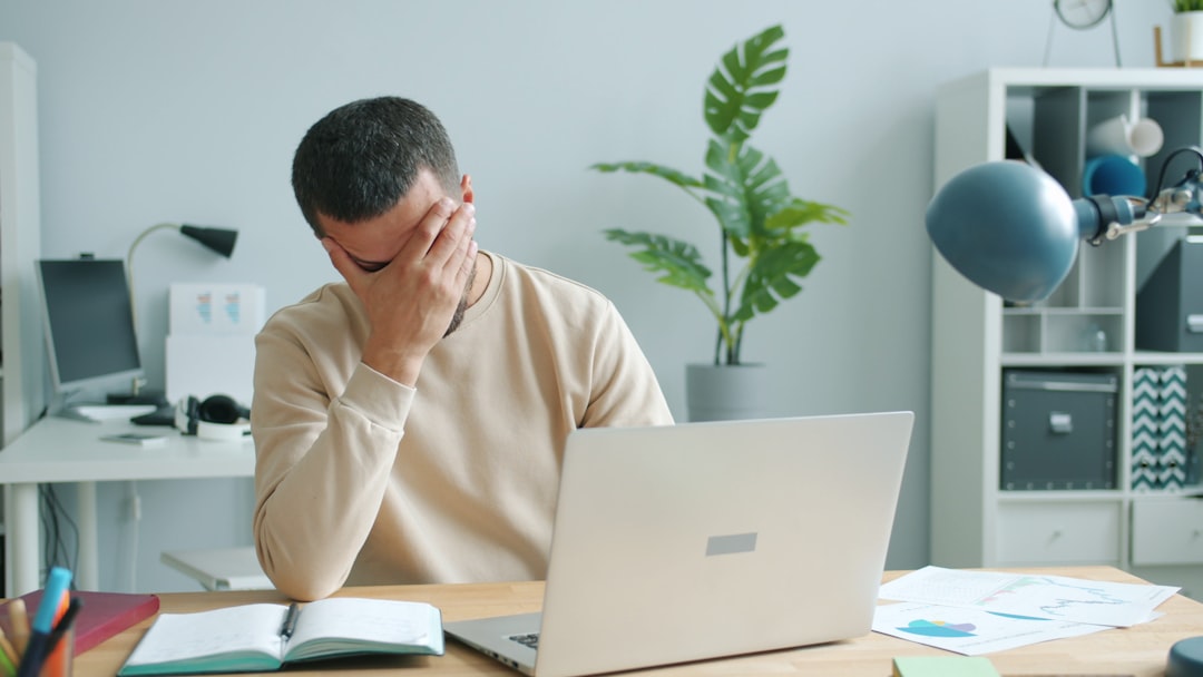 Man rubbing his face in front of laptop. business person frustrated at laptop, gst error screen, office desk documents