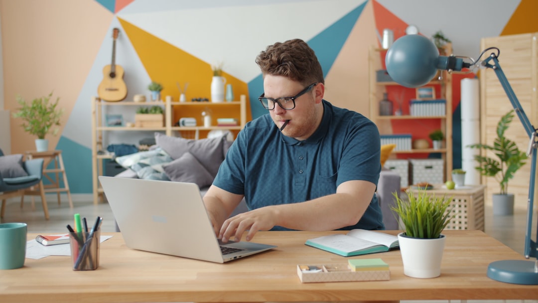 Man working on laptop at a colorful home office desk. person working from home, laptop healthcare coding, home office workspace, relaxed professional