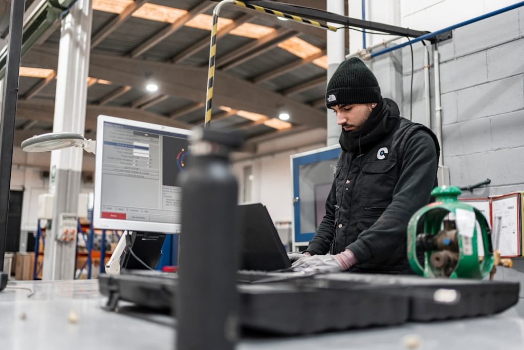 Man works on a computer in a manufacturing setting. technician wearing smart glasses, augmented reality interface, industrial maintenance environment