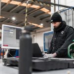 Man works on a computer in a manufacturing setting. technician wearing smart glasses, augmented reality interface, industrial maintenance environment