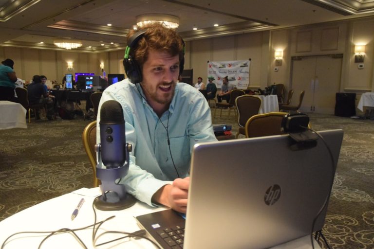 smiling man using grey HP laptop computer on desk webinar host speaking, live chat reactions, virtual networking table