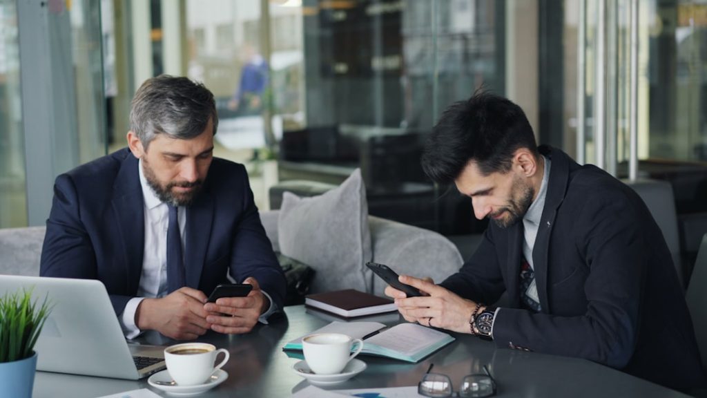 two men sitting at a table looking at their phones loan officer meeting client, mobile mortgage app, mortgage consultation office