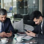 two men sitting at a table looking at their phones loan officer meeting client, mobile mortgage app, mortgage consultation office