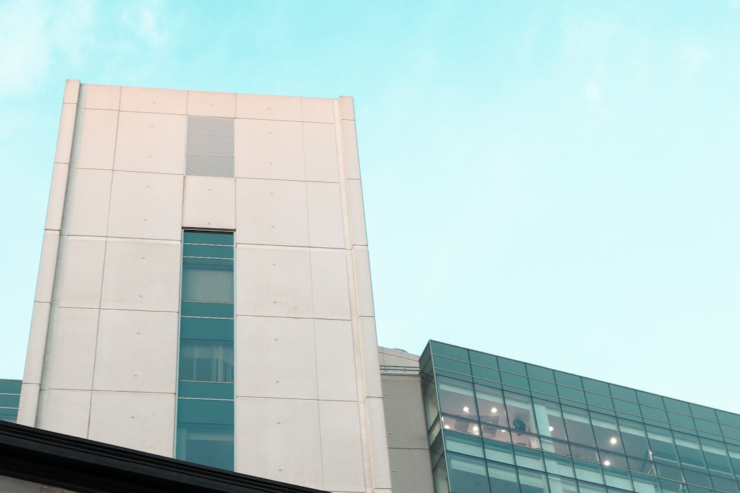 white concrete building under blue sky during daytime hospital building exterior, healthcare professionals walking, modern medical center, busy environment