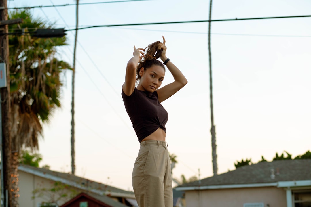 woman in black tank top and beige pants standing on electric wire during daytime 1970s California suburb, teenage girl portrait, vintage sunlight