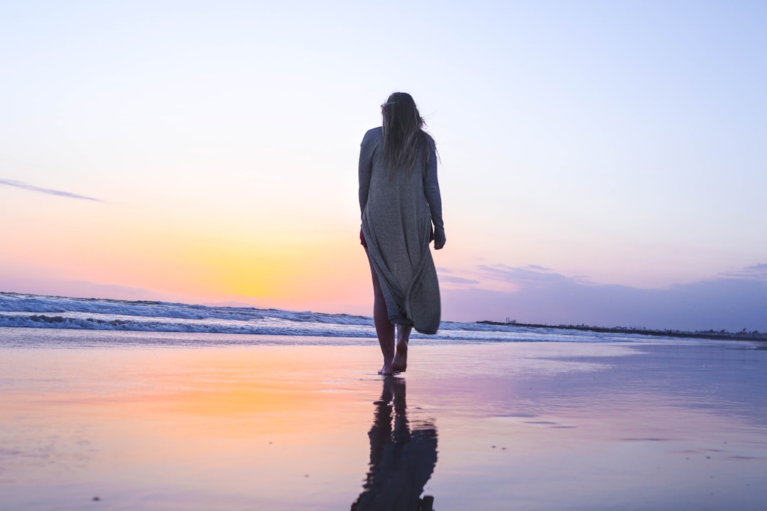 woman standing on beachfront middle aged woman walking beach at sunset, peaceful ocean background, reflective mood