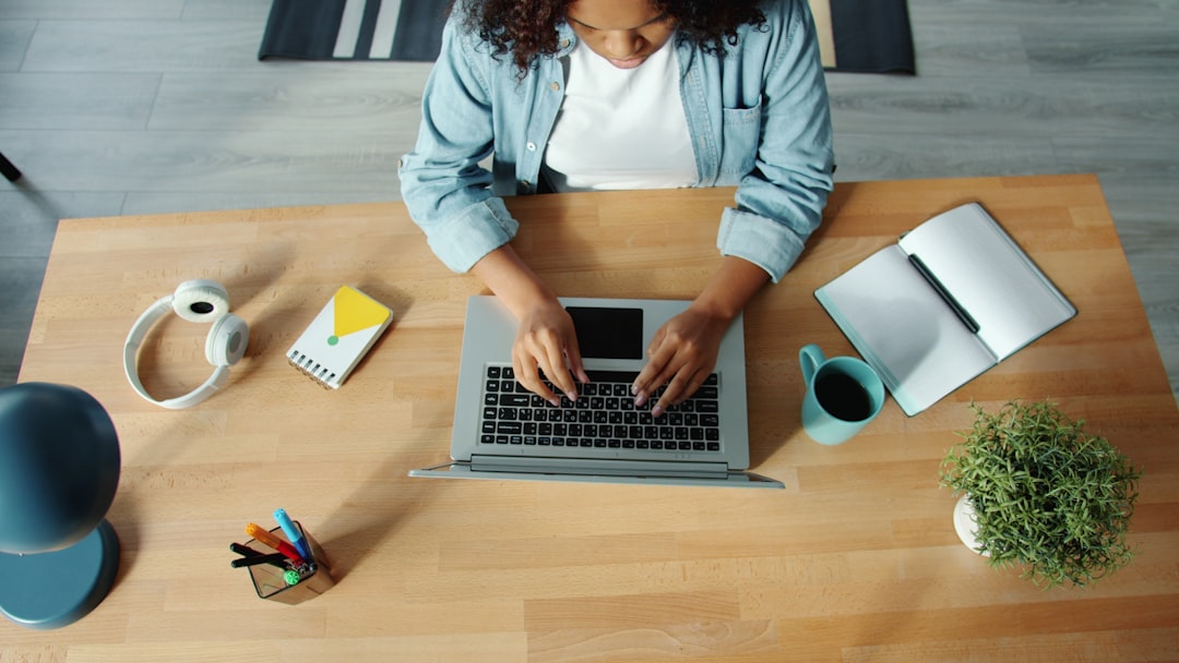Woman typing on laptop at a wooden desk. person searching jobs on laptop at home office, notebook and coffee on desk, focused workspace