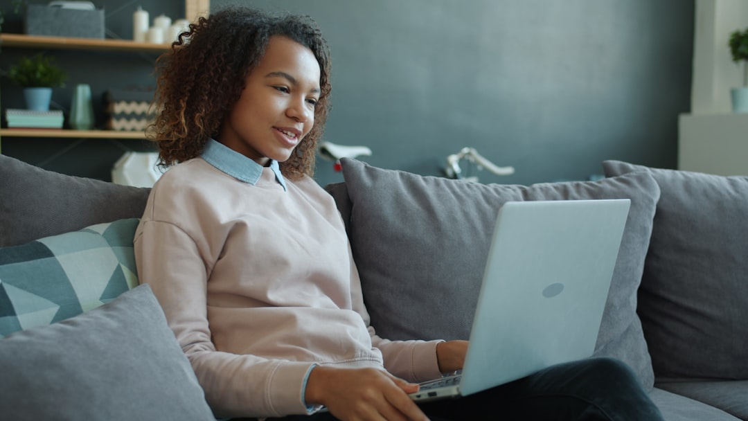 Young woman smiling while using a laptop on the couch. online doctor appointment laptop, digital health dashboard, modern living room