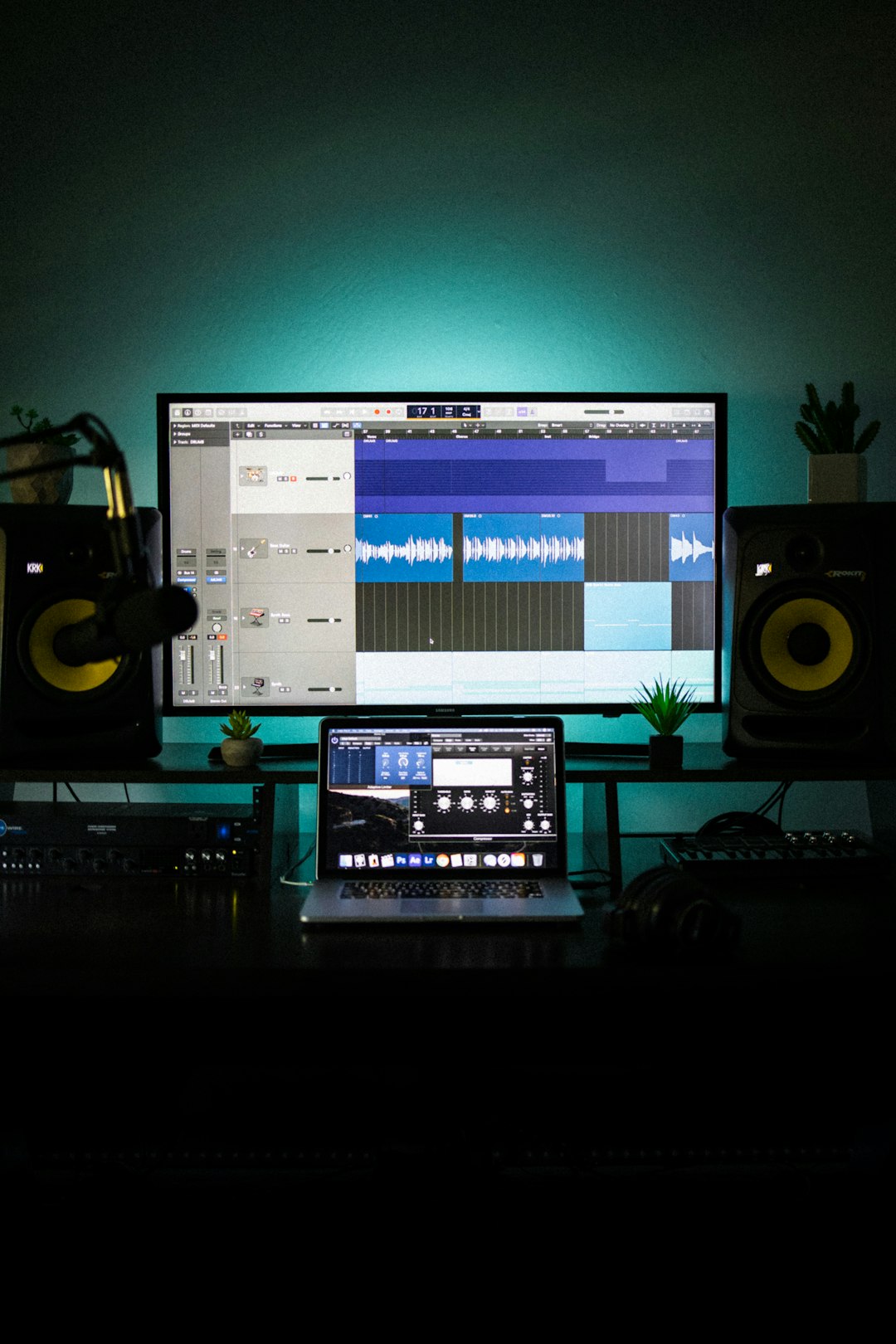 A computer monitor and laptop displaying music production software in a dark workspace command line, audio conversion, waveform