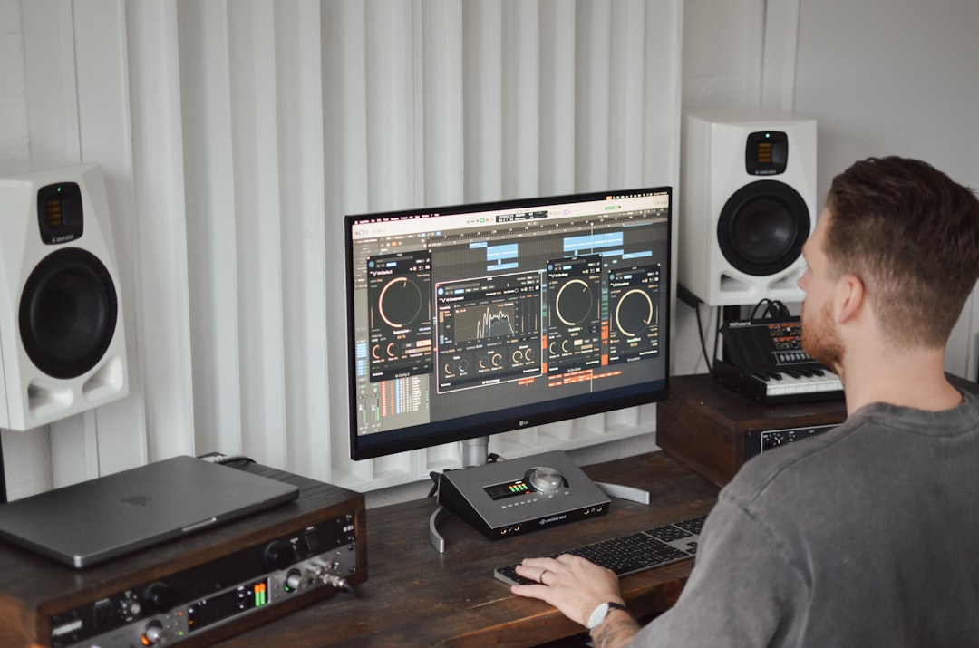 A man sitting at a desk in front of a computer home music studio setup, mac computer with daw, studio monitors and midi keyboard