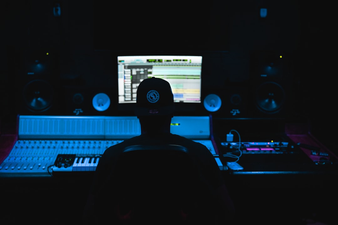 a man sitting in front of a computer in a dark room music production software interface, digital audio workstation screen, electronic music setup