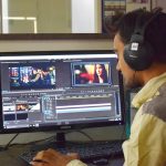 a man sitting in front of a computer with headphones on creative professional editing video, desktop editing software, cinematic footage on screen