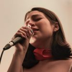 A woman sings into a microphone, eyes closed. singer posture, relaxed shoulders, vocal practice
