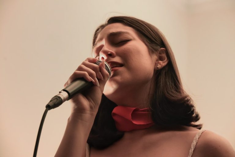 A woman sings into a microphone, eyes closed. singer posture, relaxed shoulders, vocal practice