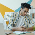 Man working at a desk with laptop and notebook. professional reviewing resume on tablet, modern office setting, career planning concept