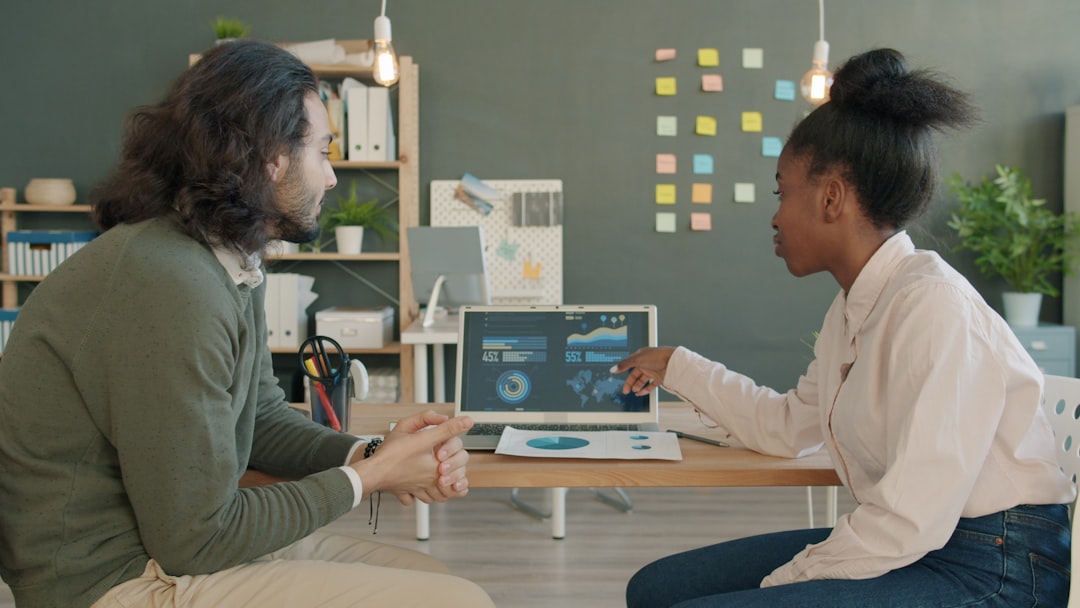 Two colleagues discussing data on a laptop screen. marketing team analyzing data, conversion rate optimization meeting, website performance metrics