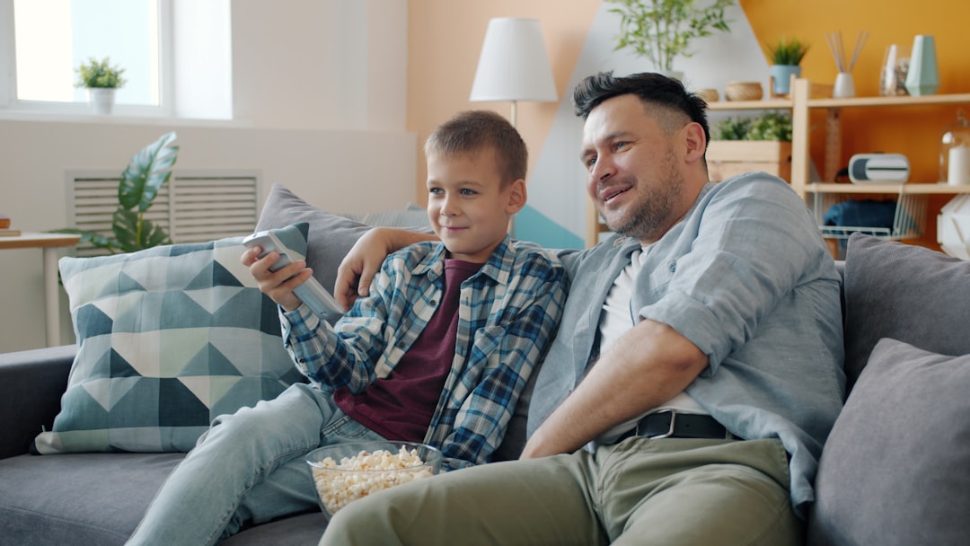 Father and son watching television together on couch. family movie night, popcorn, streaming service, sofa