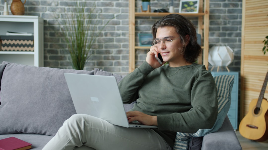 Man talking on phone while using laptop on couch cloud security, remote workers, identity protection