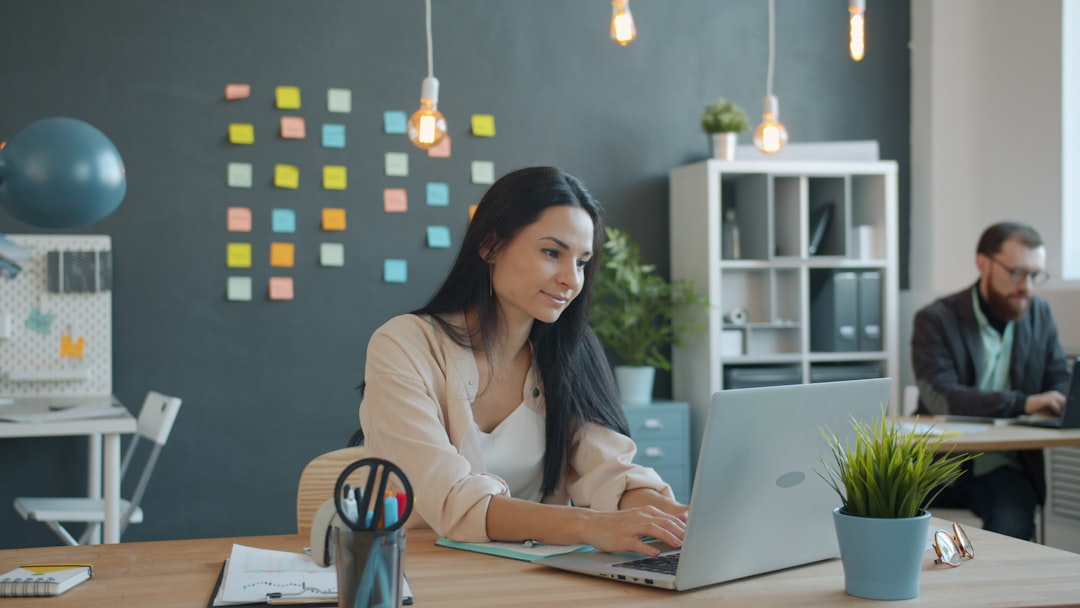 Woman working on laptop in modern office space remote team, chat messages, collaboration workspace