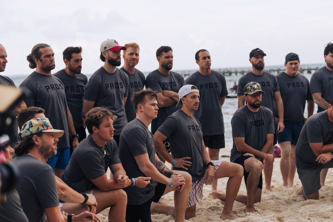 A group of men in matching shirts on a beach. team challenge, outdoor activity, coworkers solving clues, summer event