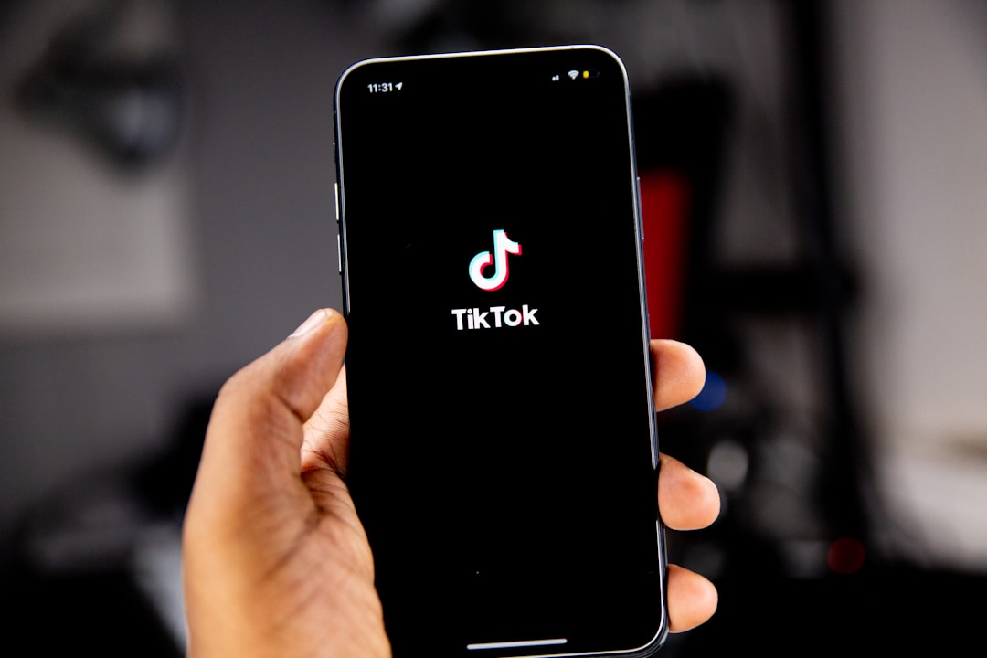 A hand holding a smartphone displaying the TikTok logo on a black screen tiktok dashboard, video metrics, creator analytics