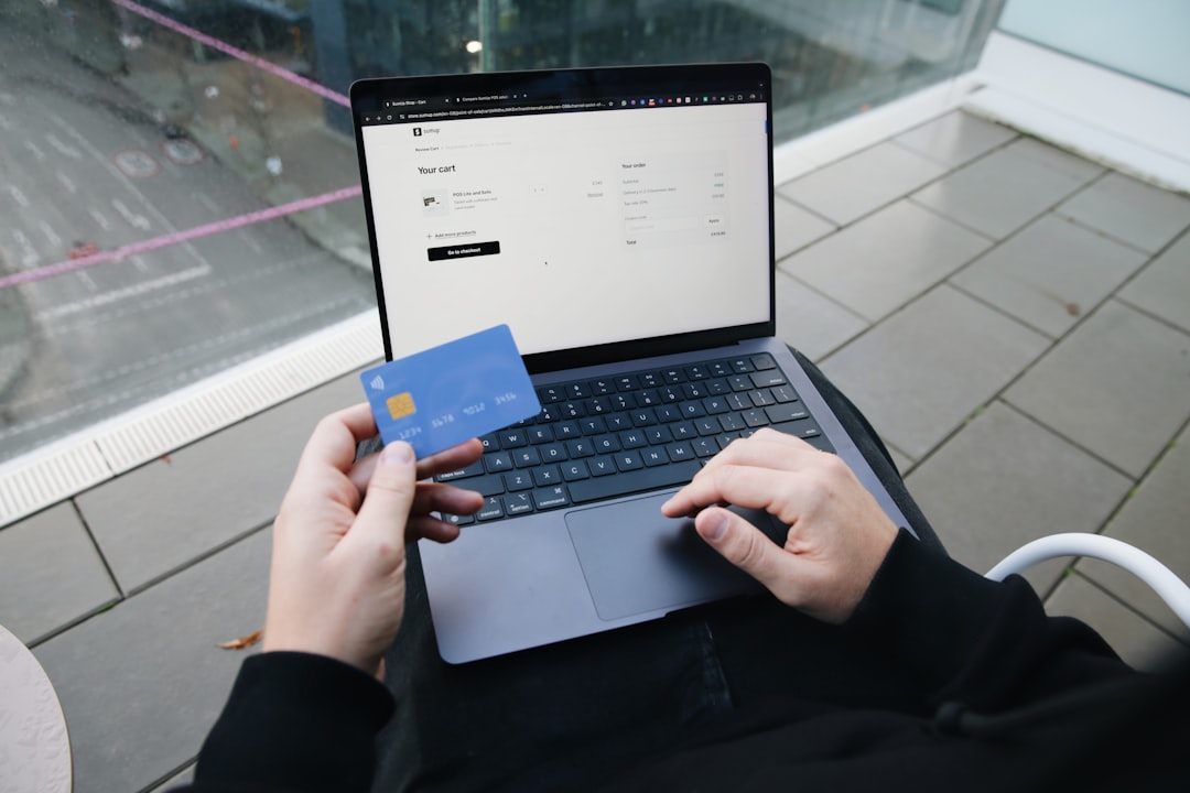 A person sitting in a chair with a laptop and a credit card global payments, currencies, secure transaction