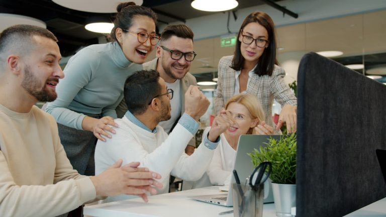 Diverse team celebrating success at office desk. happy team, delivery train, software launch, success
