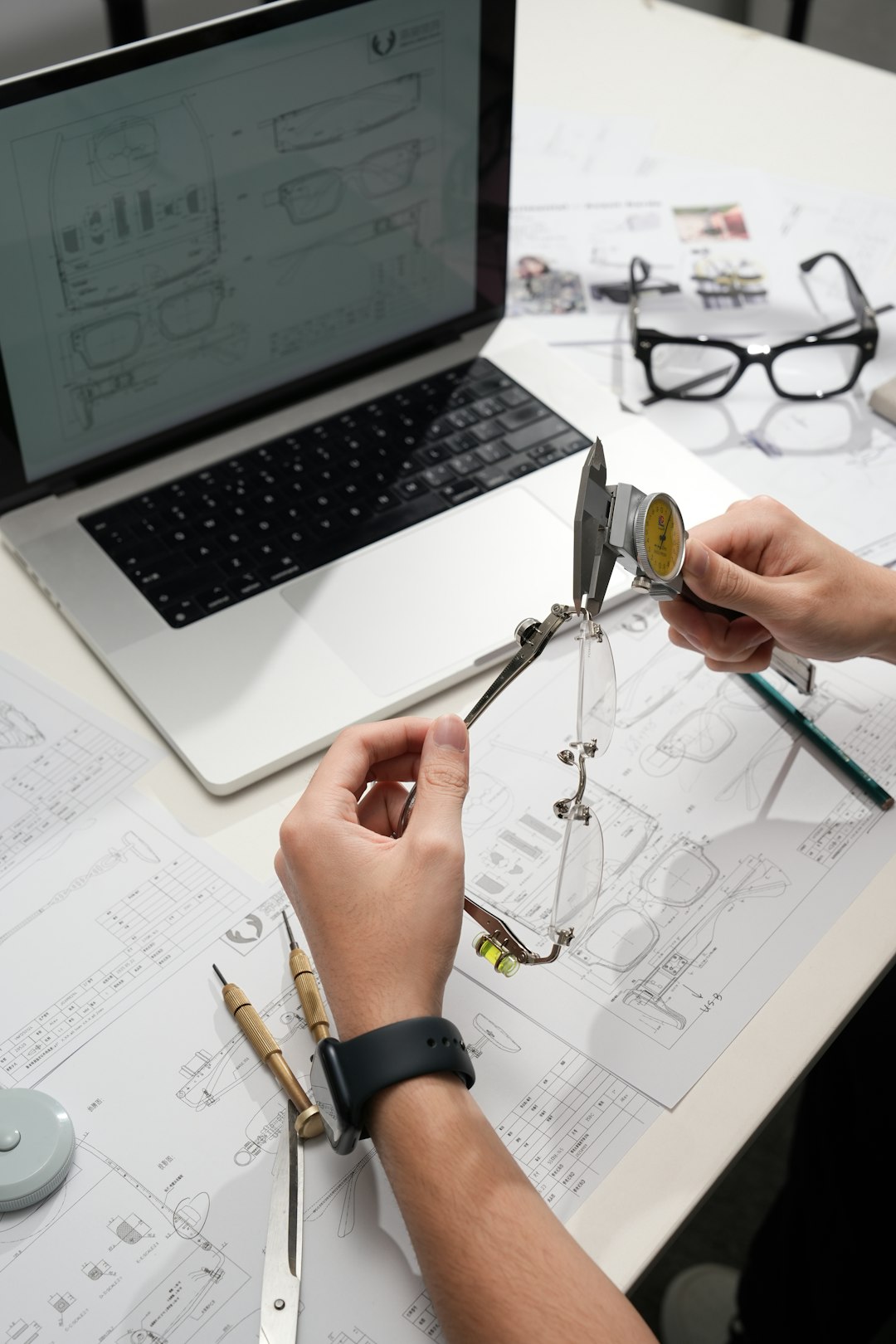 Hands measuring eyeglasses with calipers on desk product design, quality process, engineering team