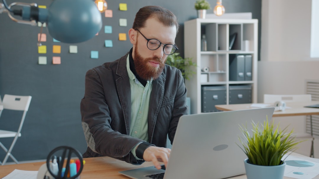Man with beard working on laptop in office small business marketing, social media content, visual workflow