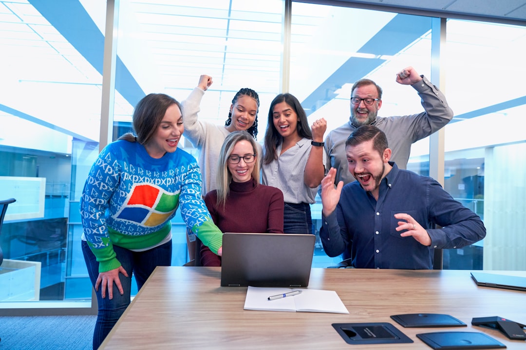 men and women sitting and standing by the table looking happy while staring at laptop happy team, delivery train, software launch, success