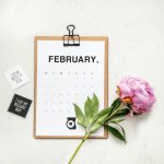 minimalist photography of a calendar and pink-petaled flower february email calendar, newsletter planning, marketing desk