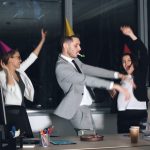 People in party hats dancing in an office at-work celebration. employee recognition, virtual meeting, team appreciation, workplace celebration
