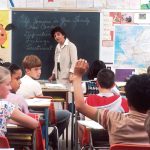 woman standing in front of children students classroom teacher books