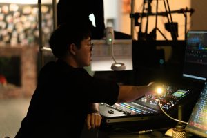 A person adjusting controls on a sound mixing board. event control room, production team, live show cues