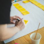 person holding white paper near white ceramic mug on brown wooden table project planning, team meeting, roadmap, sticky notes
