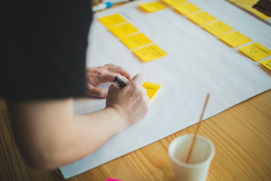 person holding white paper near white ceramic mug on brown wooden table project planning, team meeting, roadmap, sticky notes