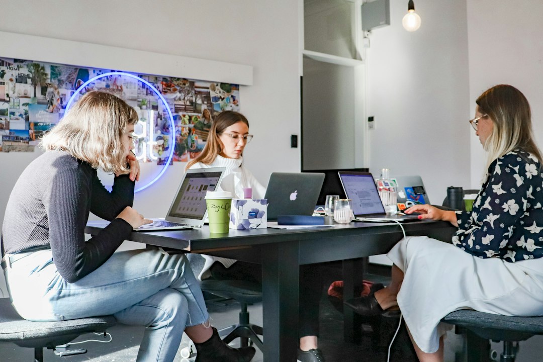 3 women sitting on chair in front of table with laptop computers cloud workflow, brand data, team dashboard