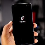 A hand holding a smartphone displaying the TikTok logo on a black screen tiktok dashboard, video metrics, creator analytics