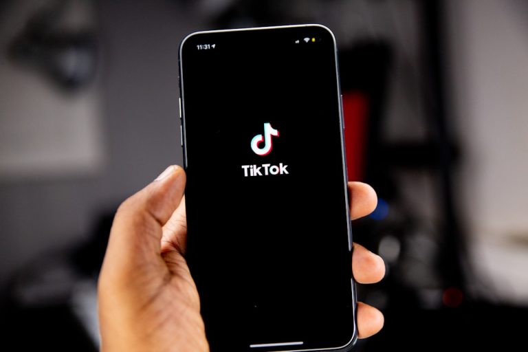 A hand holding a smartphone displaying the TikTok logo on a black screen tiktok dashboard, video metrics, creator analytics