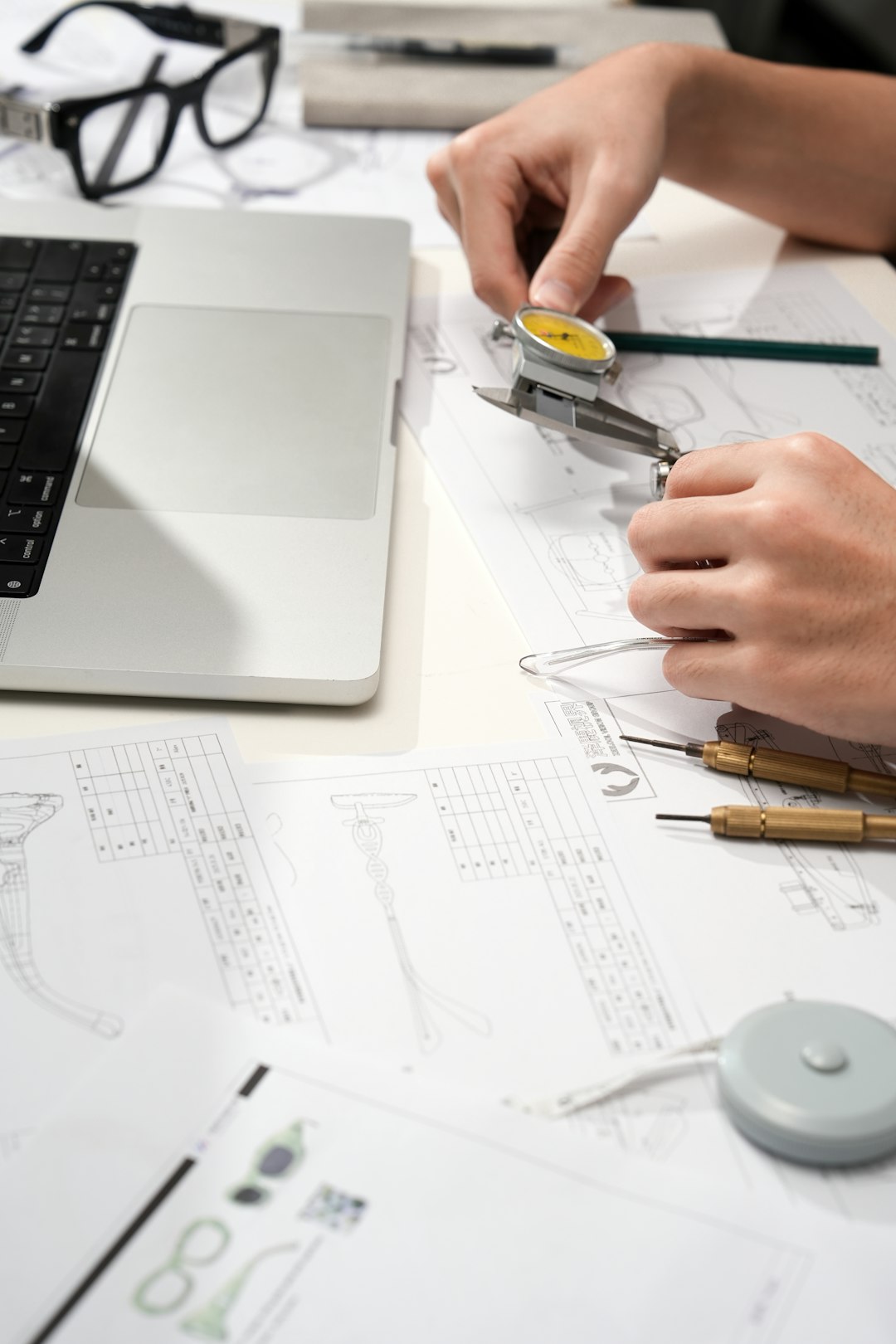 A person using a dial caliper to measure technical drawings on a desk product design, quality process, engineering team