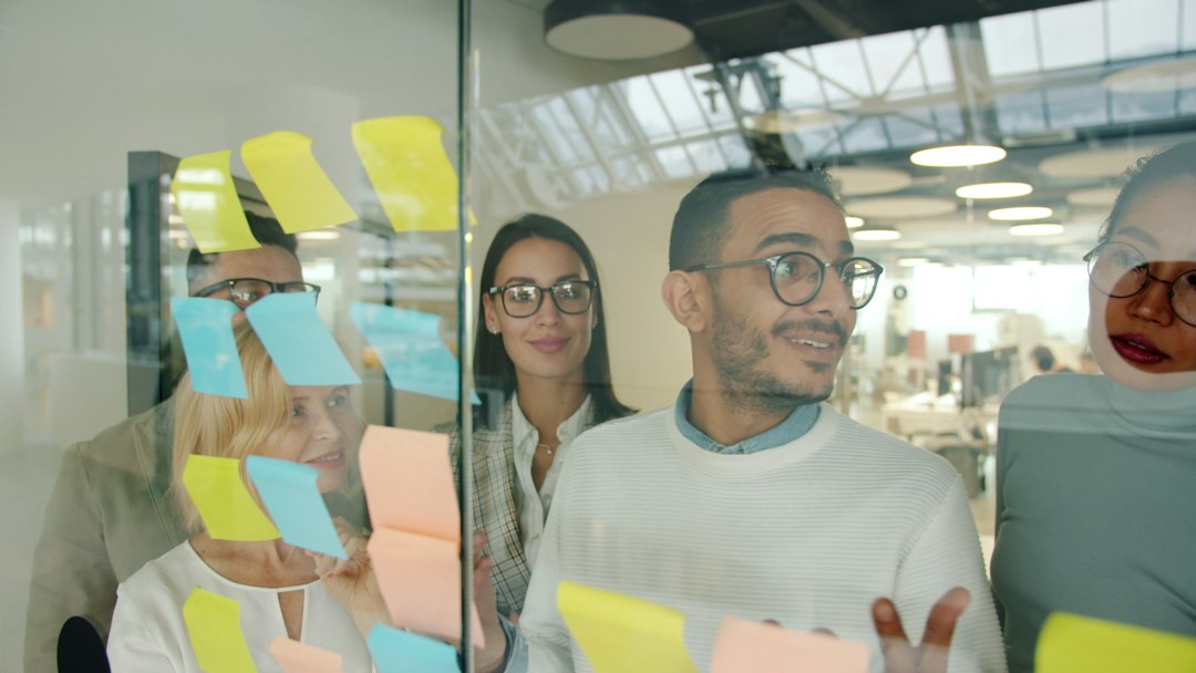 Diverse team brainstorming with sticky notes on glass team voting, whiteboard, name ideas, happy coworkers