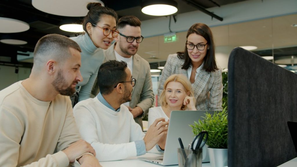 Diverse team collaborating around a laptop in office team dashboard, meeting analytics, task tracking