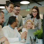 Diverse team collaborating around a laptop in office team dashboard, meeting analytics, task tracking