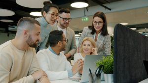 Diverse team collaborating around a laptop in office team dashboard, meeting analytics, task tracking