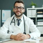 Doctor wearing a stethoscope sits at a desk doctor dictation, medical chart, clinic computer