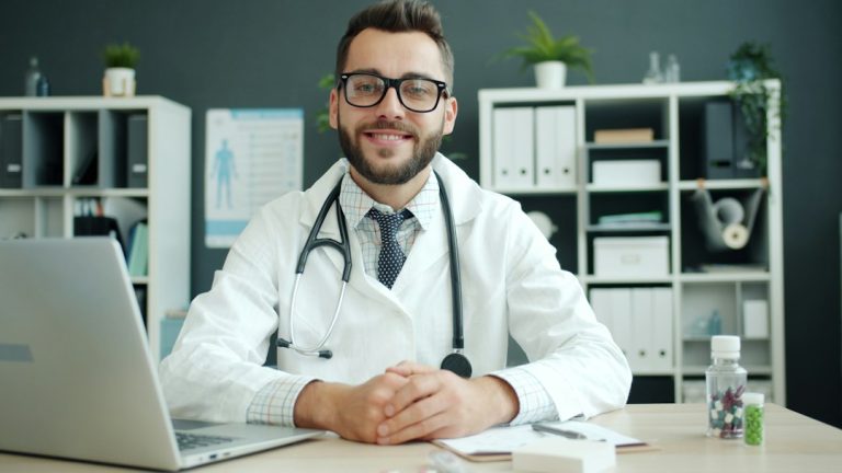 Doctor wearing a stethoscope sits at a desk doctor dictation, medical chart, clinic computer