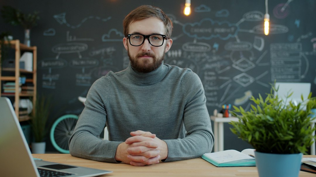 Man with glasses sitting at desk in office small business owner, email comparison, office desk