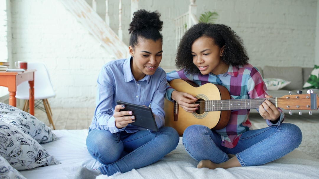 Two young women learning guitar from tablet phone video editor, caption tools, beginner creator