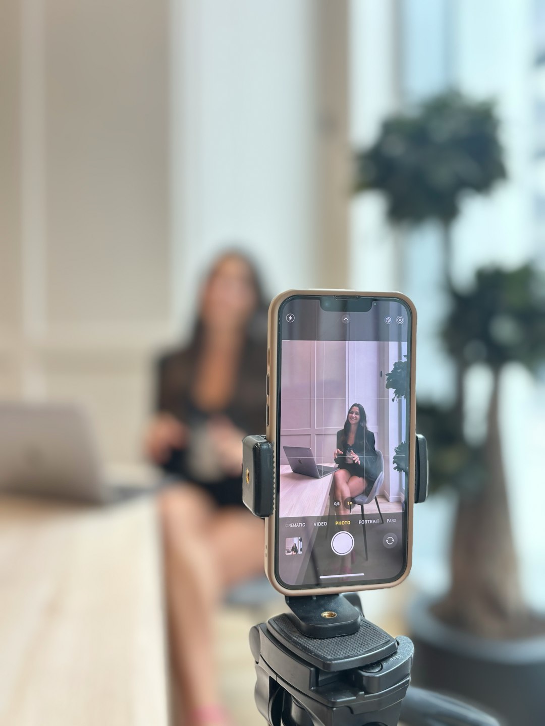 Woman recording herself on smartphone in office creator planning reel, content checklist, phone tripod
